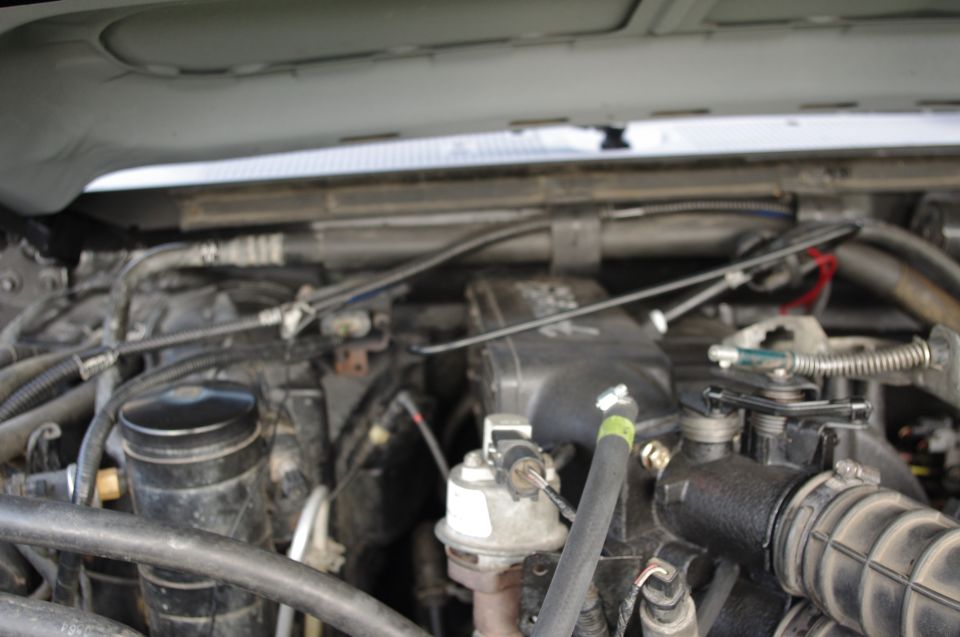 Engine bay with hoses, wires, and black plastic components. Watermark reads SUPERMOTORS