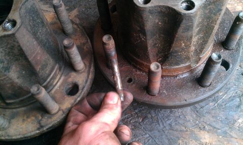 1995 Ford Bronco - Close-up of two rusty wheel hubs with lug bolts, one is held by a hand.