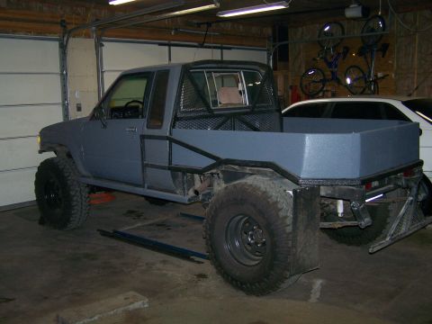 1988 Suzuki Samurai - A heavily modified pickup truck with a flatbed and roll cage sits in a garage.