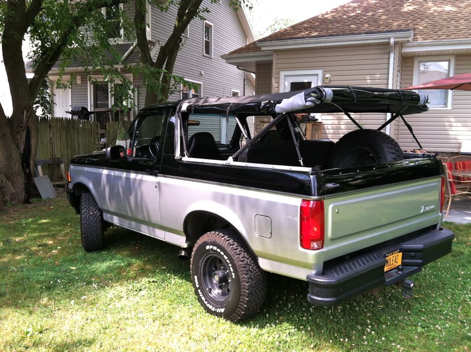 Two-tone silver and black 1992 Ford Bronco with a soft top removed, parked on grass