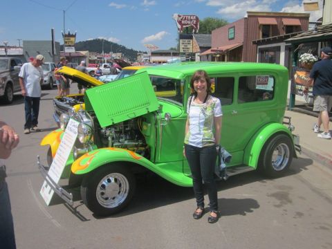 1991 Ford LTD Crown Victoria - A woman stands next to a bright green sedan with custom flames and an open hood at a car show.