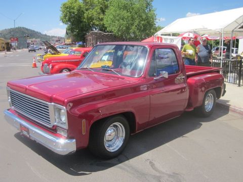 1991 Ford LTD Crown Victoria - A classic red pickup truck is displayed at an outdoor car show, with other vehicles and tents in the background.