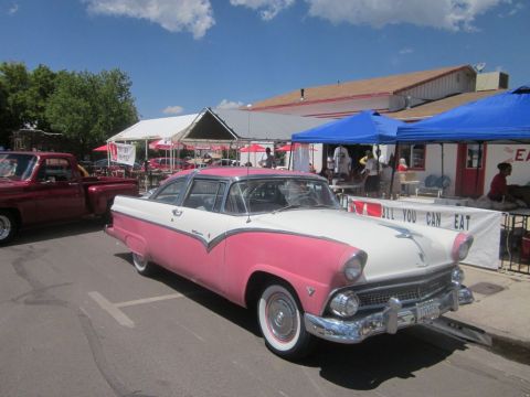 1991 Ford LTD Crown Victoria - A classic two-tone pink and white Ford Fairlane Crown Victoria is displayed at an outdoor event with a banner advertising food.