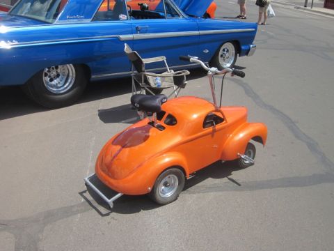 1991 Ford LTD Crown Victoria - An orange go-kart resembling a classic car is parked next to a blue vintage automobile at an outdoor car show.