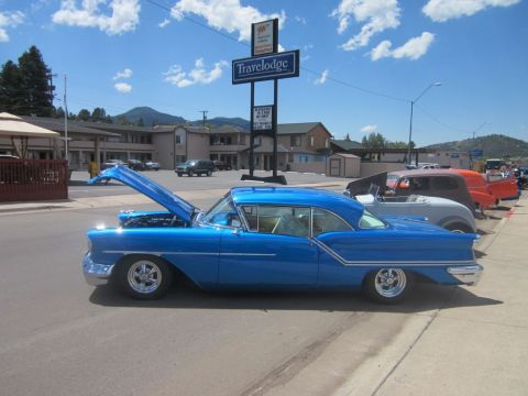 1991 Ford LTD Crown Victoria - A blue 1957 Oldsmobile Super 88 coupe is displayed with its hood open at an outdoor car show.