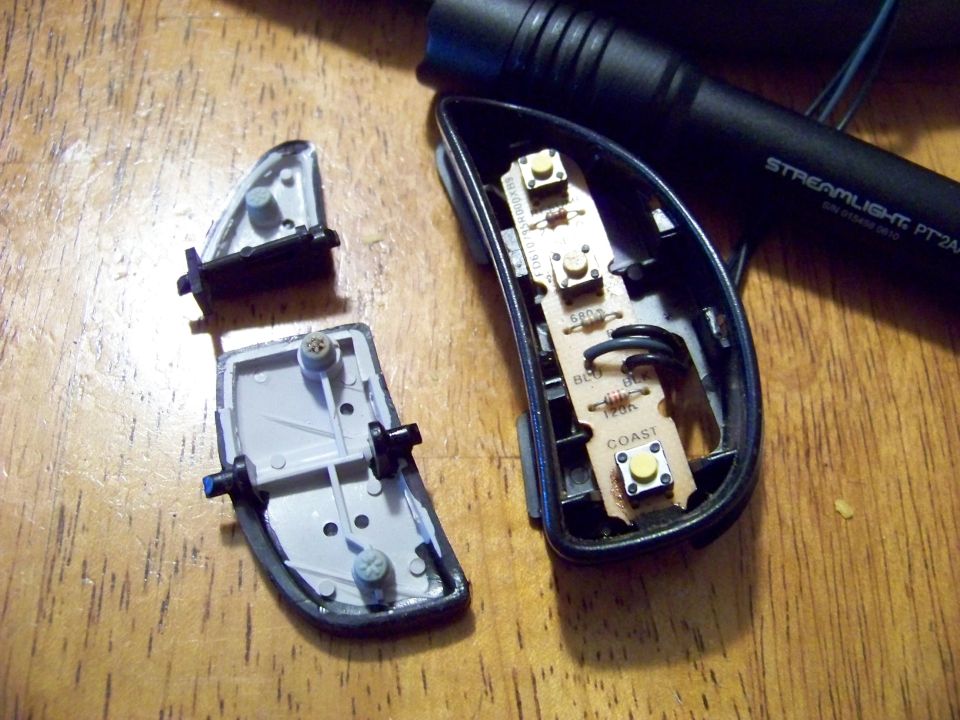 disassembled car mirror control panel with circuit board and buttons, next to a flashlight
