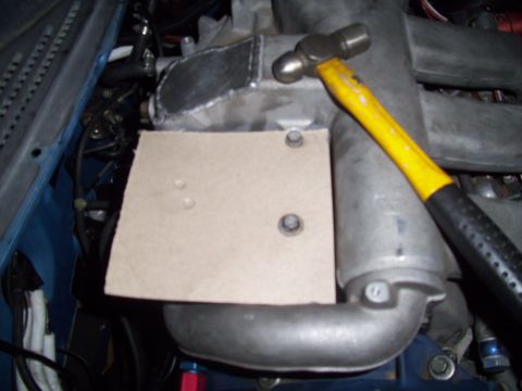 1995 Ford Probe - A ball-peen hammer is placed on an engine component covered by a bolted-on piece of cardboard.
