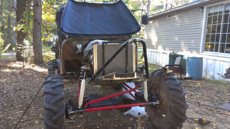 Modified off-road vehicle with hood open, showing radiator and engine bay. Large tires and roll cage are visible