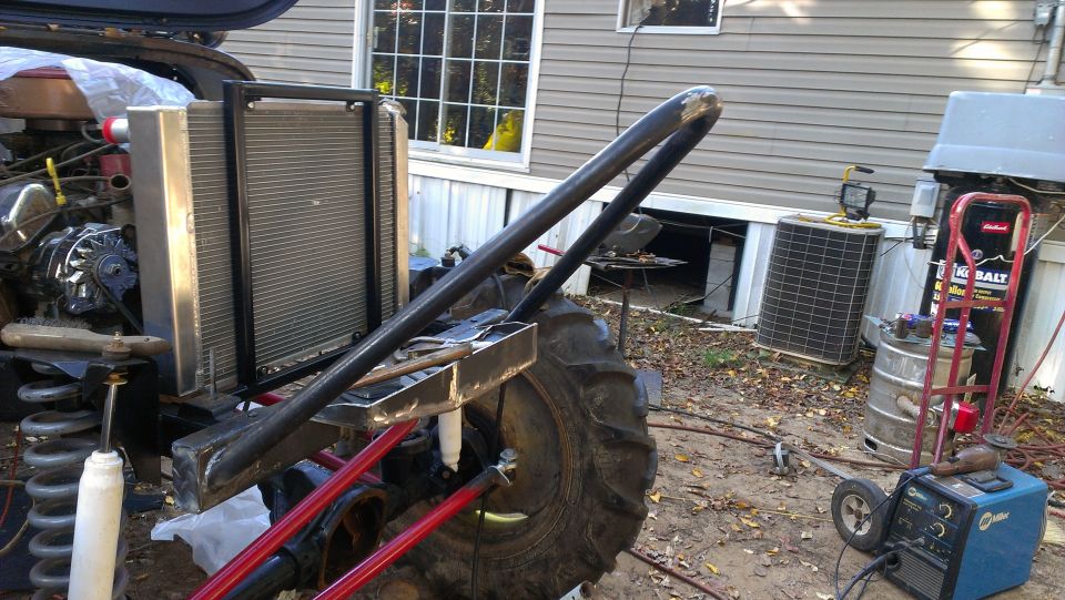 Off-road vehicle build with radiator, large tire, and roll cage tubing visible. Backyard setting with house and equipment