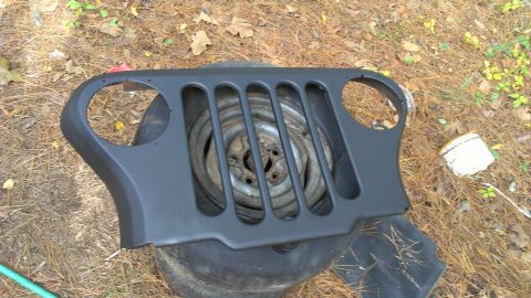 1978 Ford Bronco - A Jeep grille and spare tire are resting on the ground outdoors.