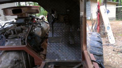1978 Ford Bronco - The interior of a vehicle shows its engine and pedals, with a diamond plate floor and exposed metal framing.