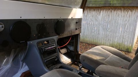1978 Ford Bronco - The interior of a vehicle shows an aftermarket stereo and speakers, with a wooden structure visible outside.