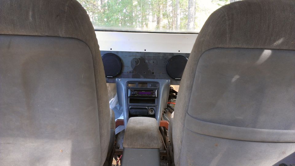 Vehicle interior with two cloth seats, center console with stereo and air vents, and speakers mounted on the dashboard