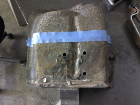 1993 Ford F-150 - A close-up view of a heavily rusted metal component, secured with blue tape, resting on a surface in a workshop.