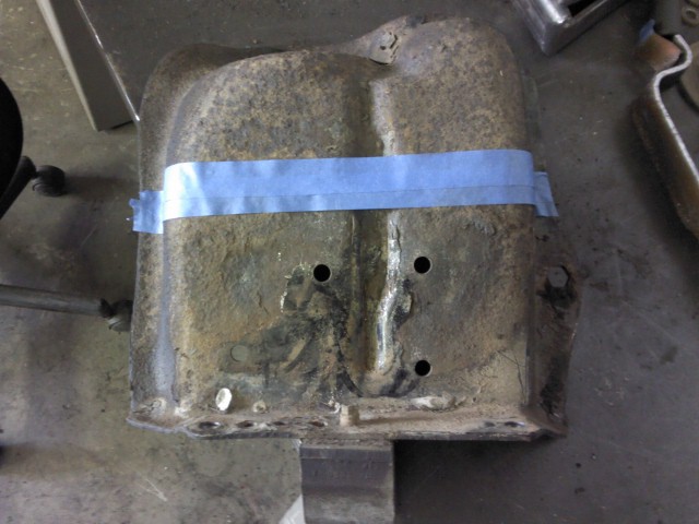 rusted metal part held together with blue tape, sitting on a workbench