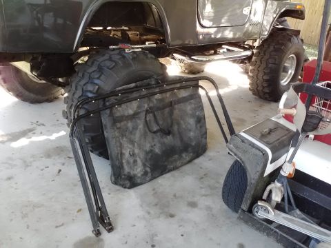 1978 Ford Bronco - A gray SUV with oversized tires is parked next to a lawn bag and a golf cart.