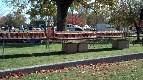 2007 Ford Mustang - Numerous trophies are displayed on tables outdoors, with parked cars and trees visible in the background.