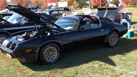 2007 Ford Mustang - Black 1977 Pontiac Firebird Trans Am at a car show with hood open, showing engine details.