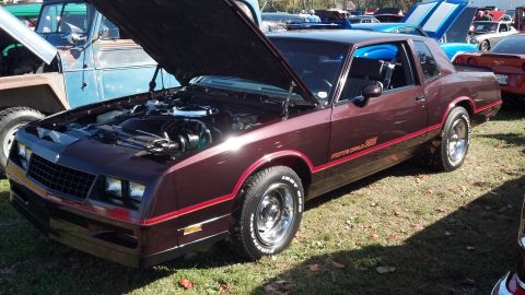 2007 Ford Mustang - Maroon 1980s Chevrolet Monte Carlo SS with hood open, parked next to a blue Jeep at an outdoor event.