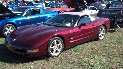 2007 Ford Mustang - A red convertible sports car is parked on grass next to other vehicles at an outdoor event.