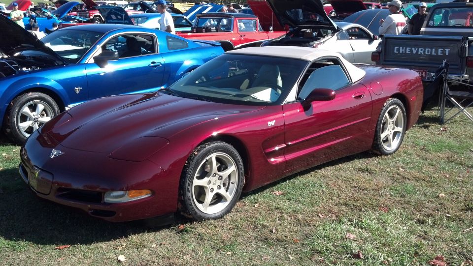 Red convertible sports car with a tan top, parked on grass. Visible side and front quarter panel