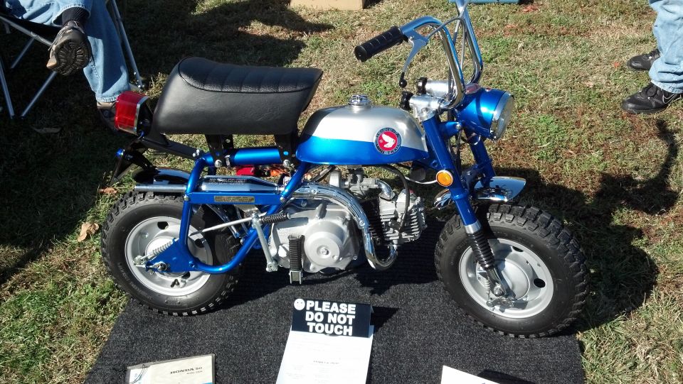 Blue and silver Honda Z50 minibike with "PLEASE DO NOT TOUCH" sign
