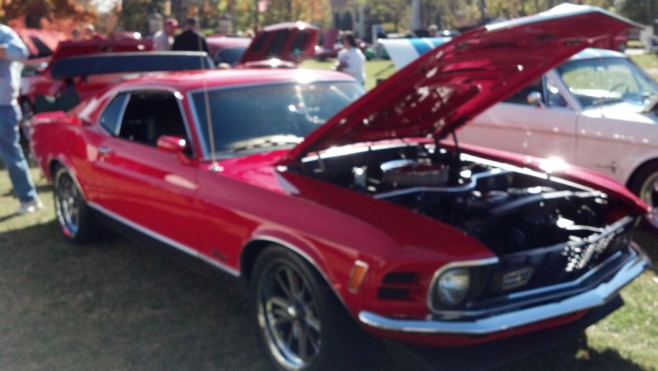 Red classic coupe with hood open, showing engine. Another classic car is parked to the right