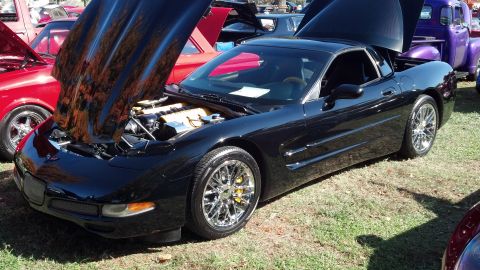 2007 Ford Mustang - Black Chevrolet Corvette C5 with hood open at an outdoor car show, parked on grass.
