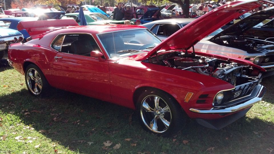 Red 1970s Ford Mustang coupe with hood open, chrome wheels, and a large rear spoiler