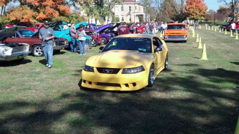 2007 Ford Mustang - A yellow Ford Mustang is displayed at an outdoor car show with other vehicles and spectators present.