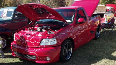 2007 Ford Mustang - Custom red pickup truck with lightning graphics on display at an outdoor car show.