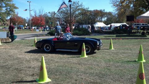 2007 Ford Mustang - A black convertible sports car is parked on a grassy field, with people and tents in the background.