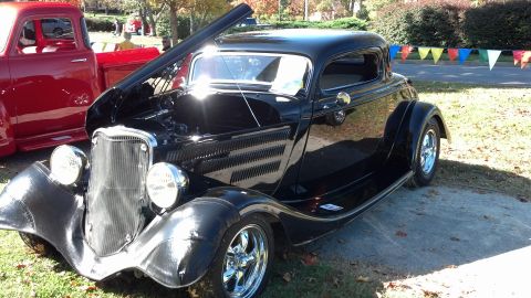 2007 Ford Mustang - A black coupe hot rod is displayed with its hood open, parked beside a red pickup truck at an outdoor event.