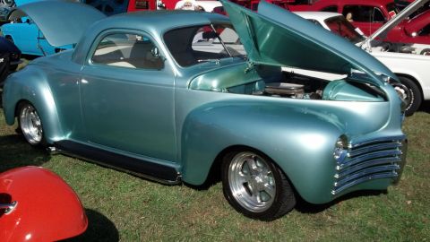 2007 Ford Mustang - A teal coupe with its hood open, displaying custom wheels and a chrome grille, sits on a grassy field with other vehicles.