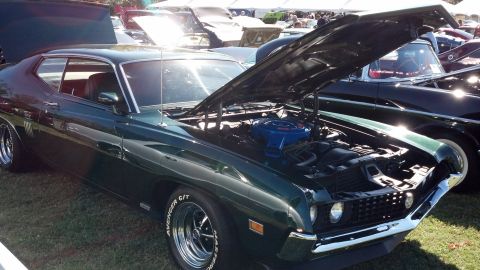 2007 Ford Mustang - A dark green coupe from the 1970s is displayed with its hood open, revealing the engine and tires with "AVENGER G/T" lettering.