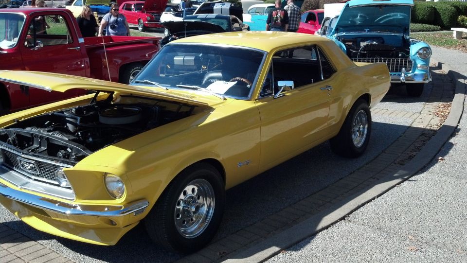 Yellow 1967 Ford Mustang coupe with hood open, parked next to other vehicles