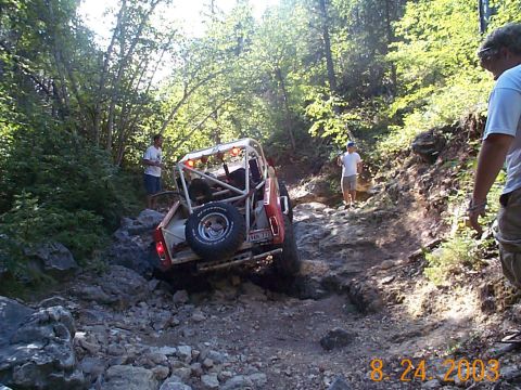 1977 Ford Bronco - Off-road vehicle navigates a challenging rocky path in a wooded area.