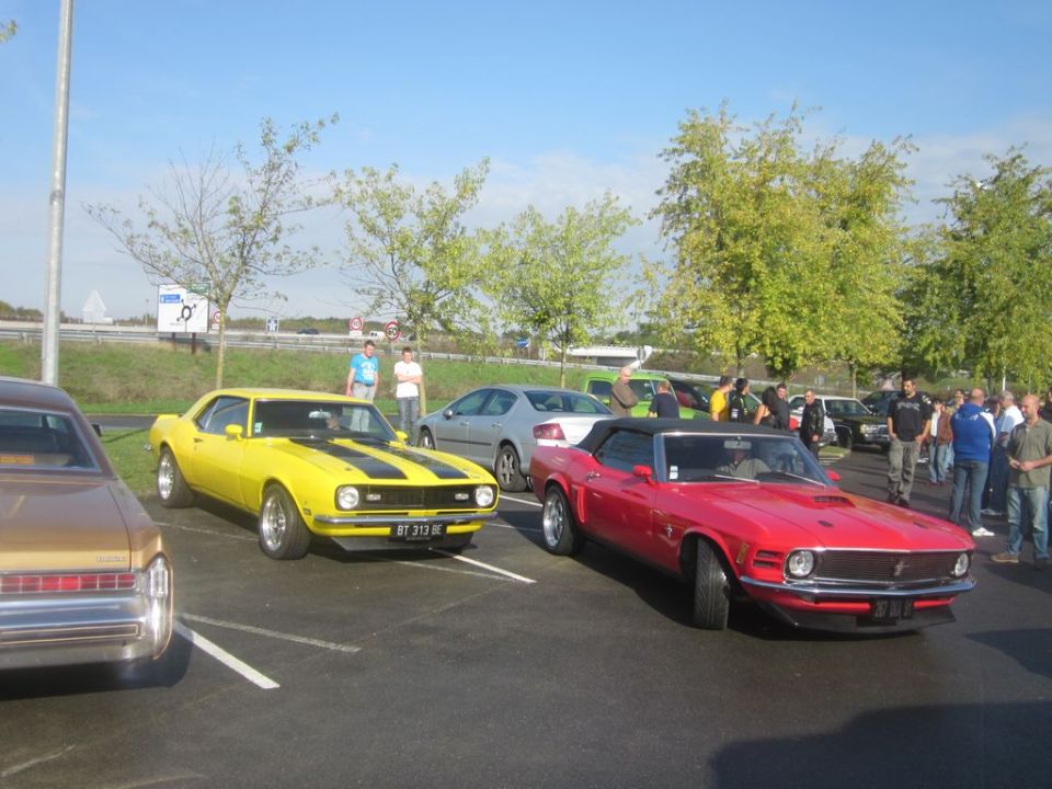 Yellow 1960s Chevrolet Camaro with black stripes parked next to a red convertible Ford Mustang