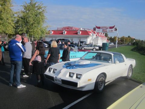 1991 Ford LTD Crown Victoria - A group of people stand around a white Pontiac Firebird Trans Am at an outdoor car gathering.