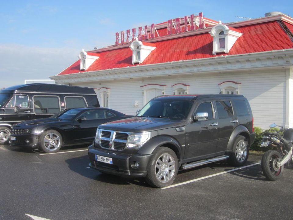 Dark gray Dodge Nitro parked next to a black Chevrolet Camaro and a black van. A motorcycle is parked to the right