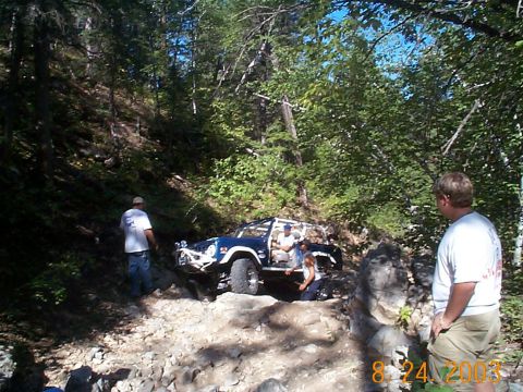 1977 Ford Bronco - A blue off-road SUV navigates a challenging rocky terrain with onlookers present.