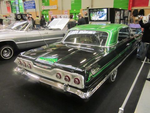 1991 Ford LTD Crown Victoria - A customized 1964 Chevrolet Impala with green accents is displayed indoors next to another classic car.