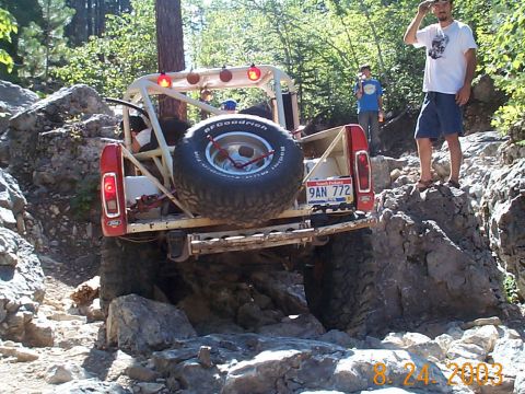 1977 Ford Bronco - A heavily modified pickup truck, possibly a custom build, navigates a challenging rocky trail with a spare tire mounted at the rear.
