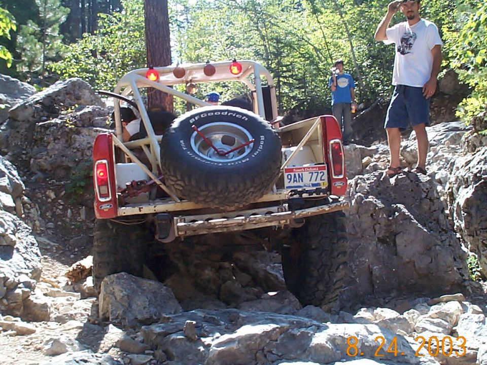 Rear view of a modified pickup truck with a spare tire and roll cage, navigating rocky terrain
