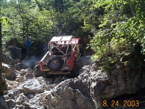 1977 Ford Bronco - Off-road vehicle tackling a challenging rocky path in a wooded area.