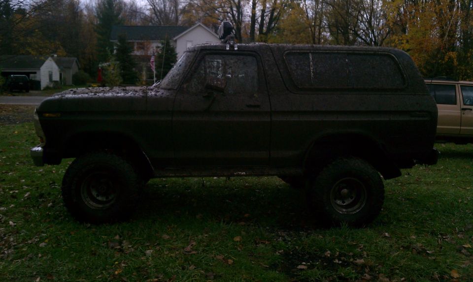 Mud-covered 1978 Ford Bronco side profile, parked on grass with another vehicle behind it
