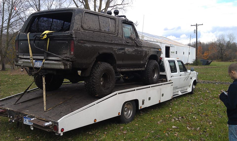 Mud-covered 1979 Ford Bronco on a flatbed tow truck, rear 3/4 view