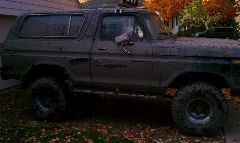 1979 Ford Bronco - This heavily soiled SUV, likely a 1978 Ford Bronco, sits parked with fallen leaves scattered around its tires.