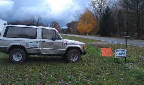 1979 Ford Bronco - A silver SUV is parked on a grassy area next to a road, with signs indicating an off-road park.
