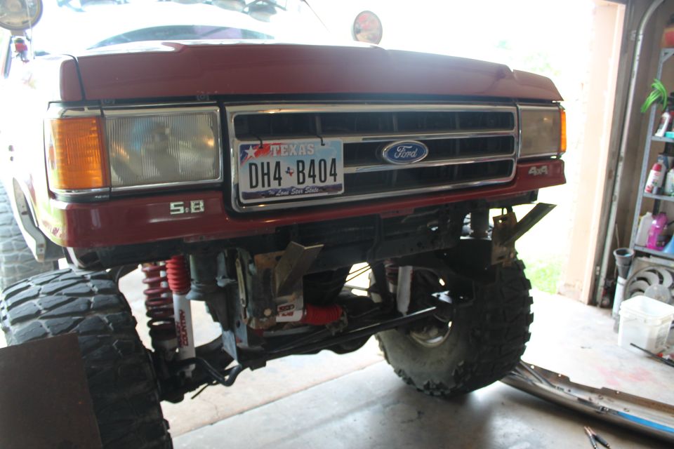 Front of a red Ford F-Series truck with a lifted suspension and large tires. Texas license plate DH4-B404 is visible